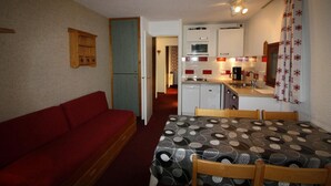 A compact living space with a red sofa, a dining table with patterned tablecloth, and a kitchenette with a microwave, stove, and coffee maker. - 150m from ski lifts, 1st floor, balcony, tv, ski locker, 40m², Tignes (Tignes)