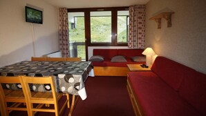 A room with a dining table, red sofa, and a TV mounted on the wall. - 150m from ski lifts, 1st floor, balcony, tv, ski locker, 40m², Tignes (Tignes)