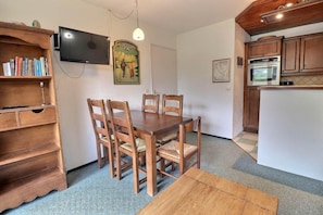 A dining area with a wooden table and chairs, a bookshelf, a television, and a kitchen with wooden cabinets and appliances. - 10m from ski slopes, Ground floor, balcony, 40m², Méribel-Mottaret (Méribel - Les Allues)