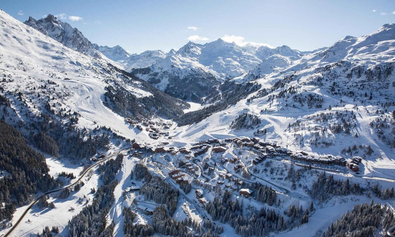 A snow-covered mountain village with winding roads and buildings nestled among trees.