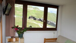 Une pièce avec un lit en bois, une petite table, une plante en pot et une fenêtre donnant sur un paysage montagneux.