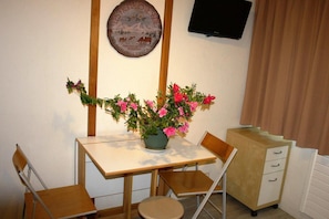 A small dining area with a table, chairs, a vase of flowers, a wall-mounted plate, and a television.
