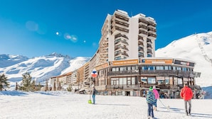 Un bâtiment d’une station de ski doté de nombreux balcons et de panneaux indiquant « École de ski français » et « Banque Populaire ».