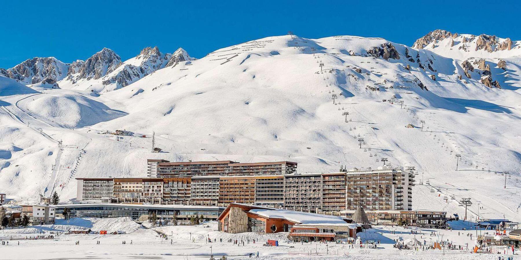 Un hôtel à plusieurs étages, avec des pistes de ski en arrière-plan et un paysage montagneux.