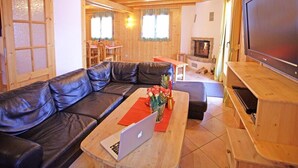 A cozy living room with a leather sofa, a wooden coffee table with a laptop, and a flat-screen TV on a wooden stand. - Chalet, 350m from ski slopes, sauna, terrace, balcony, fireplace or stove, parking, tv, ski locker (La Tzoumaz)