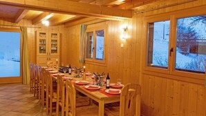 A wooden dining room with a long table set for a meal, wooden cabinets, and large windows with a snowy view. - Chalet, 350m from ski slopes, sauna, terrace, balcony, fireplace or stove, parking, tv, ski locker (La Tzoumaz)