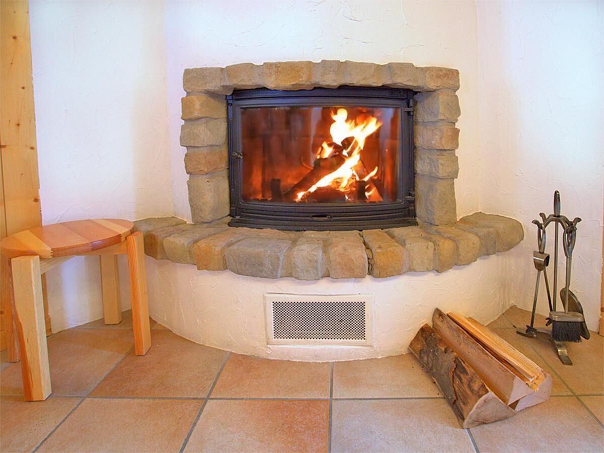Une cheminée en pierre avec un feu, une chaise en bois et un ensemble d’accessoires de foyer posé sur le sol.