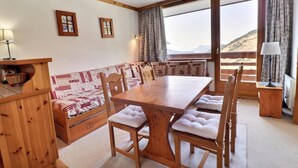 A cozy dining area with a wooden table and benches, a sofa with patterned cushions, and a view of the outdoors. - 10m from ski slopes, 9th floor, balcony, 33m², Méribel-Mottaret (Méribel - Les Allues)