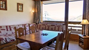 A cozy room with a wooden table, cushioned bench, and a view of mountains through large windows. - 10m from ski slopes, 9th floor, balcony, 33m², Méribel-Mottaret (Méribel - Les Allues)