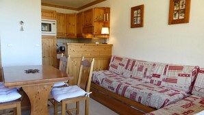 A cozy room with a wooden dining table, chairs, and a patterned sofa. - 10m from ski slopes, 9th floor, balcony, 33m², Méribel-Mottaret (Méribel - Les Allues)