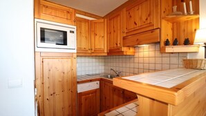 A compact kitchen with wooden cabinets, a microwave, a dishwasher, and a tiled backsplash. - 10m from ski slopes, 9th floor, balcony, 33m², Méribel-Mottaret (Méribel - Les Allues)
