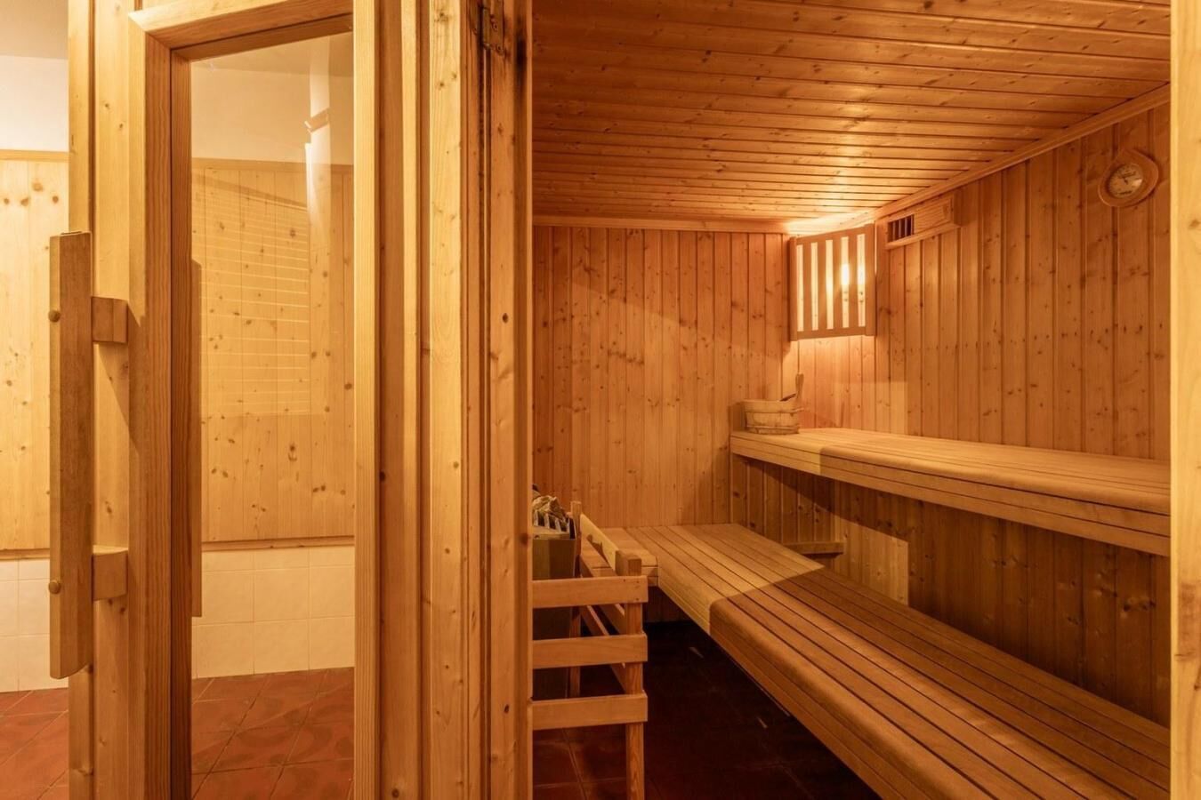 A wooden sauna with benches and a bench seat, wooden walls, and a wooden door.
