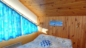 Una habitación con paneles de madera, una cama, una ventana con cortinas azules y un cuadro pequeño en la pared.
