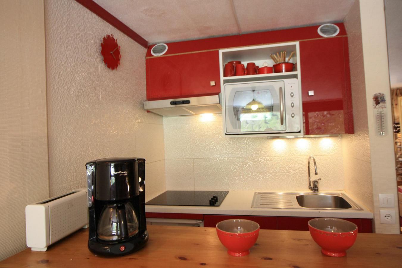 A compact kitchen with a coffee maker, two red bowls, a microwave, and a sink.