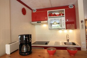 A compact kitchen with a coffee maker, two red bowls, a microwave, and a sink.