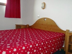 A single bed with a wooden headboard, a red bedspread with a white pattern, a small bedside table, and a wall-mounted light fixture. - 150m from ski slopes, 2nd floor, view mountain, tv, 43m², Orcières Merlette 1850 (Orcières)