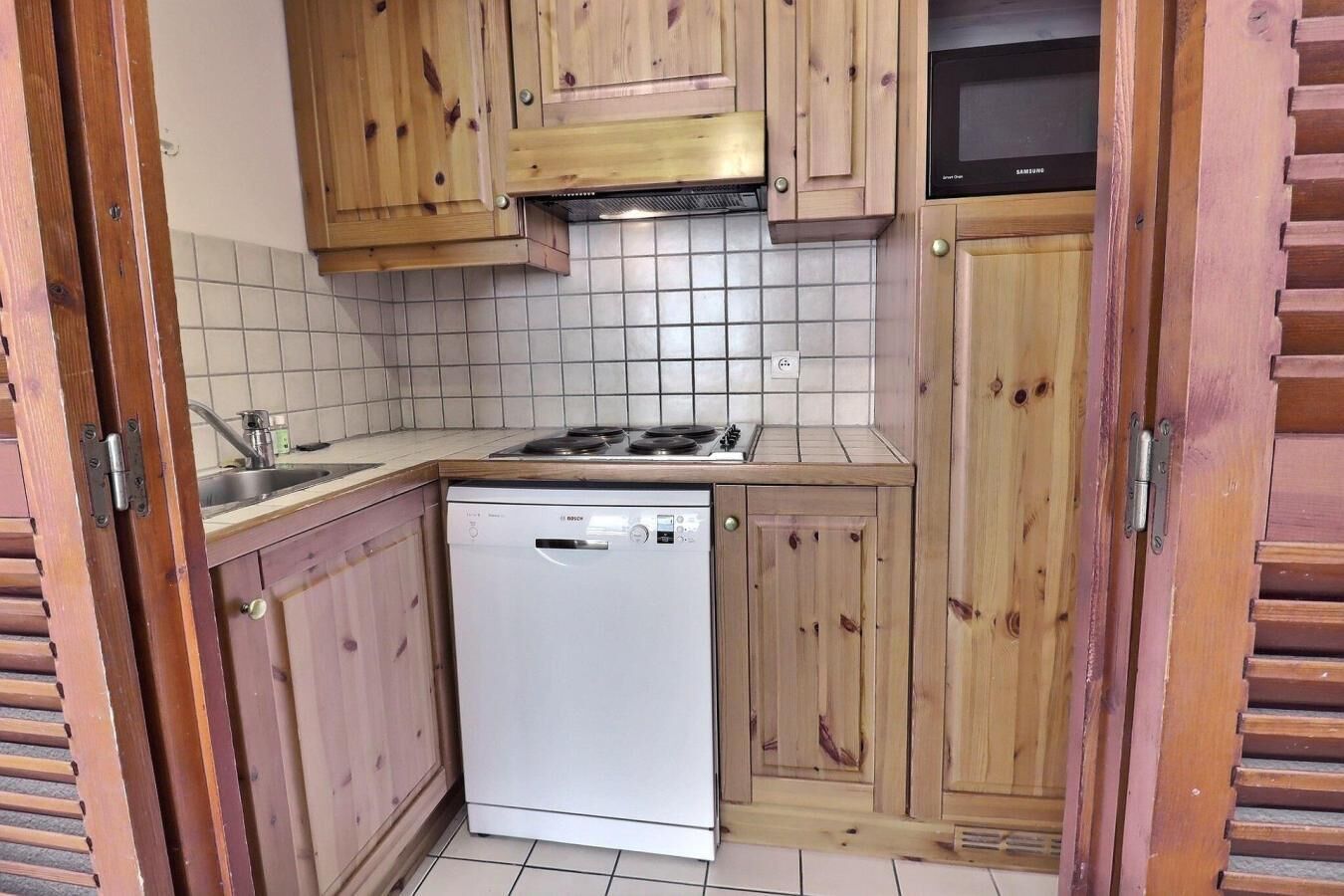 A compact kitchen with wooden cabinets, a Bosch dishwasher, a gas stove, and a microwave.
