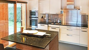 Cozinha moderna com armários brancos, bancada de granito preto, eletrodomésticos de aço inoxidável e teto de madeira.