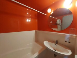 A bathroom with a white sink, a mirror, and an orange wall.