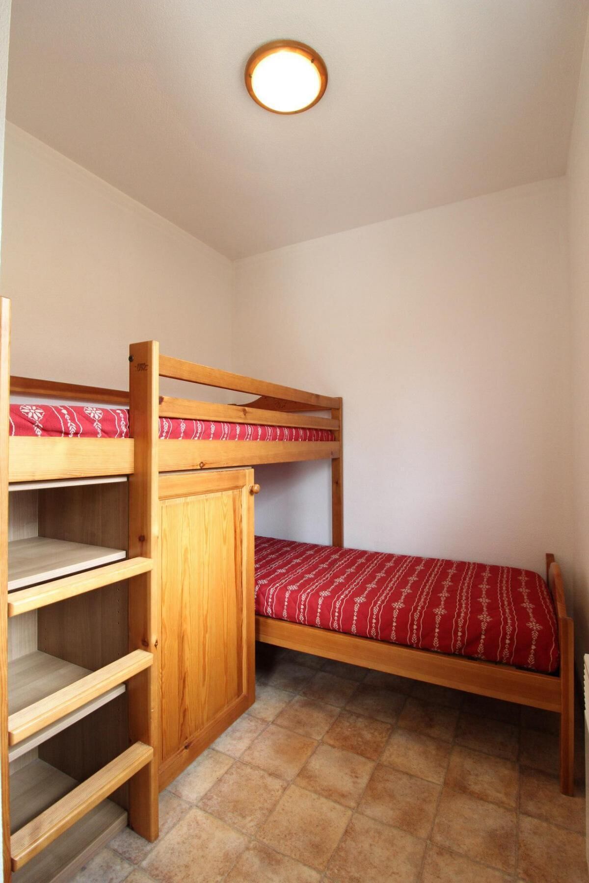 Een slaapkamer met een stapelbed, een houten kast en een enkel bed.