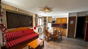 A cozy living room with a sofa, a wooden coffee table, and a dining area with chairs and a table. A kitchen area is visible in the background. - 10m from ski slopes, 1st floor, balcony, tv, ski locker, 42m², Val Cenis (Lanslevillard)