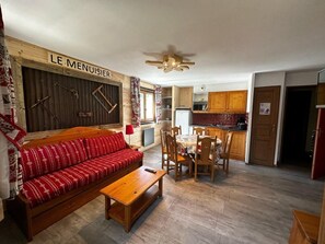 Ein gemütliches Wohnzimmer mit einer Couch, einem Holztisch und einem Essbereich mit Stühlen und einem Tisch. Im Hintergrund ist eine Küche zu erkennen.