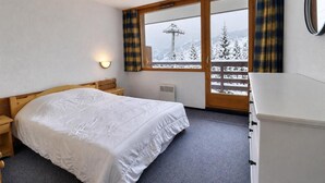 Un dormitori amb un llit, una taula de nit, una petxera, una finestra amb cortines i vistes a un paisatge nevà.