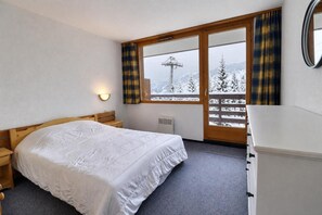 Una camera da letto con un letto, un comodino, una cassettiera, una finestra con tende e vista su un paesaggio innevato.