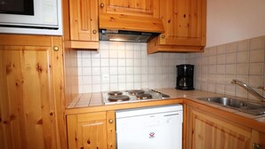 Una cuina amb armaris de fusta, un rentaplats blanc, una placa de cocció, una cafetera i un rentamànega.