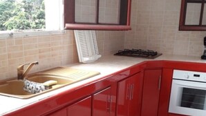 Une cuisine avec des meubles de rangement rouges, une cuisinière à gaz, un évier et une fenêtre.