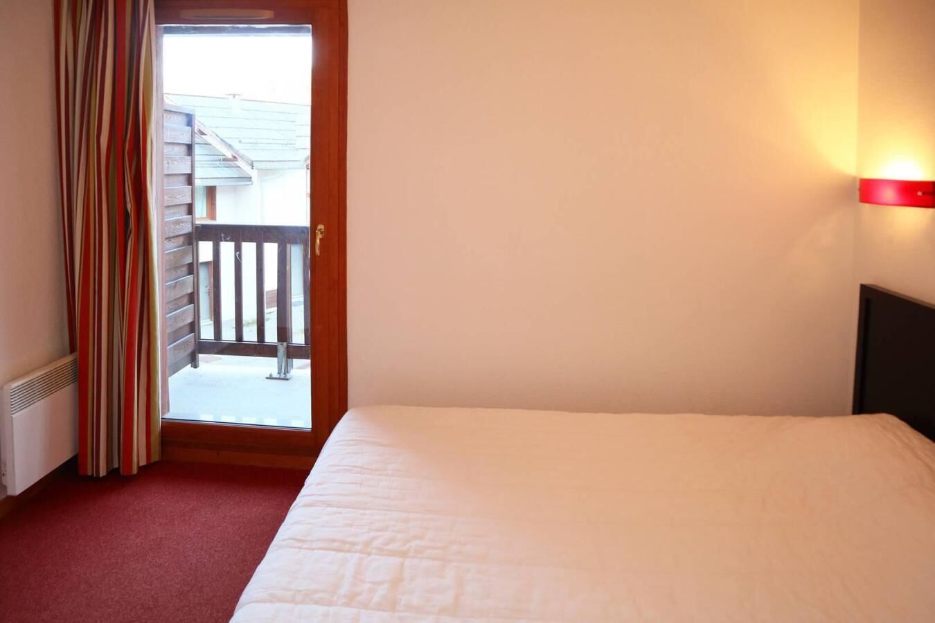 Ett hotellrum med en säng, ett fönster med gardiner och utsikt över en byggnad utanför.