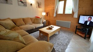Un salon chaleureux avec un plancher en bois, un canapé beige, une table basse en bois et un téléviseur posé sur un meuble.