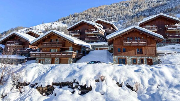 Un ensemble de chalets en bois dotés de balcons, situés au pied d’une montagne enneigée.