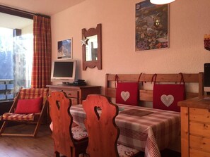 Quarto acolhedor com uma mesa de jantar de madeira, cadeiras, uma televisão e uma janela com cortinas.