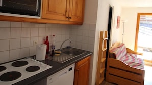 A compact kitchen with wooden cabinets, a built-in microwave, a dishwasher, and a small dining area with a wooden table and bench. - 300m from ski slopes, floor -1, view mountain, terrace, parking, tv, ski locker, 49m², Valfréjus (Valfréjus)
