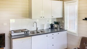 Una cocina compacta con armarios blancos, un lavamanos de acero inoxidable, una estufa y una cafetera.