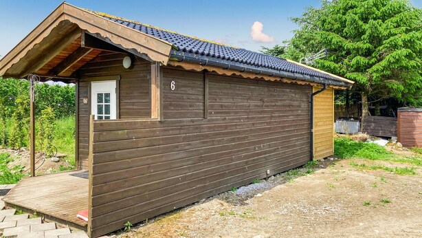 Una cabaña de madera con techo de tejas, un pequeño porche y una puerta.