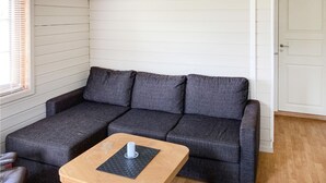 Habitación de esquina con un sofá gris, una mesita de madera y una puerta blanca.