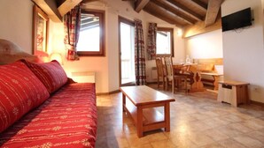 A cozy room with a red patterned sofa, a wooden table, and a dining area with chairs and a table. - 10m from ski slopes, 4th floor, balcony, tv, ski locker, 33m², Val Cenis (Lanslevillard)