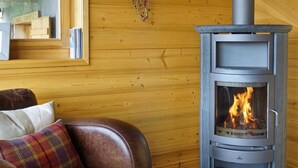 Una habitación acogedora con un sofá de cuero, un cojín escocés y una estufa de leña.