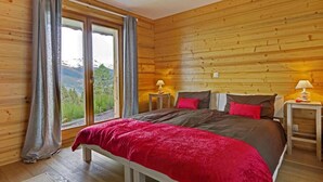 Un dormitorio con paneles de madera, una cama grande, dos mesitas de noche y vistas a la montaña a través de una ventana.