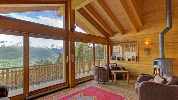 Una cabaña acogedora con amplios ventanales que ofrecen vistas a la montaña, chimenea y decoración de madera.