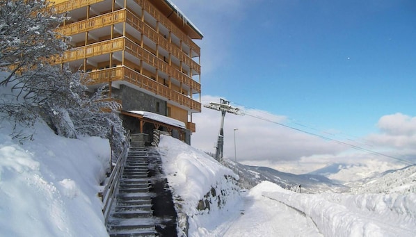 A multi-story building with balconies, a staircase leading up to it, and a snowy landscape in the background.
