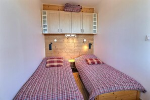 A small, cozy room with two single beds, wooden headboard, and built-in cabinets above the beds.