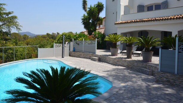 A swimming pool surrounded by a white building with a tiled roof, potted plants, and a view of distant mountains. - Luxury Villa, Pool and Beautiful View (Saint-Raphaël)