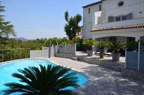 A swimming pool surrounded by a white building with a tiled roof, potted plants, and a view of distant mountains. - Luxury Villa, Pool and Beautiful View (Saint-Raphaël)