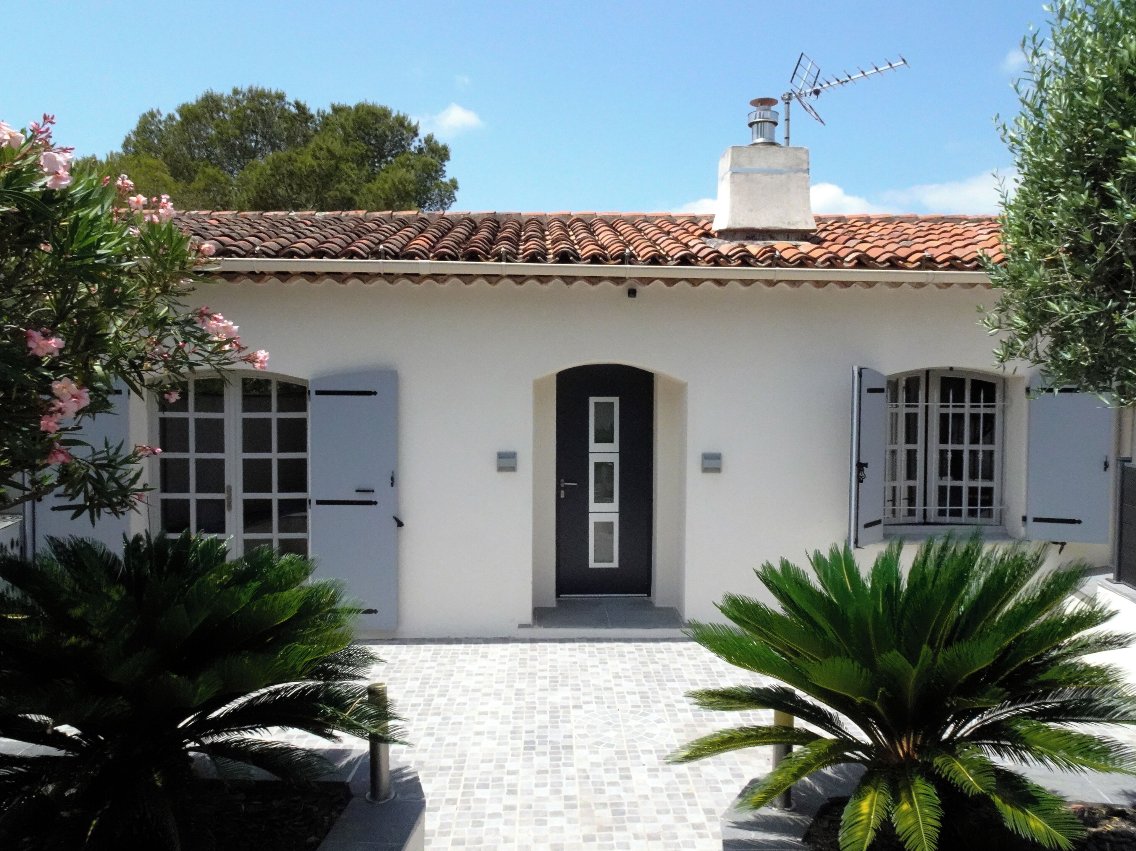 A building with a tiled roof, a central door, and two windows with shutters.