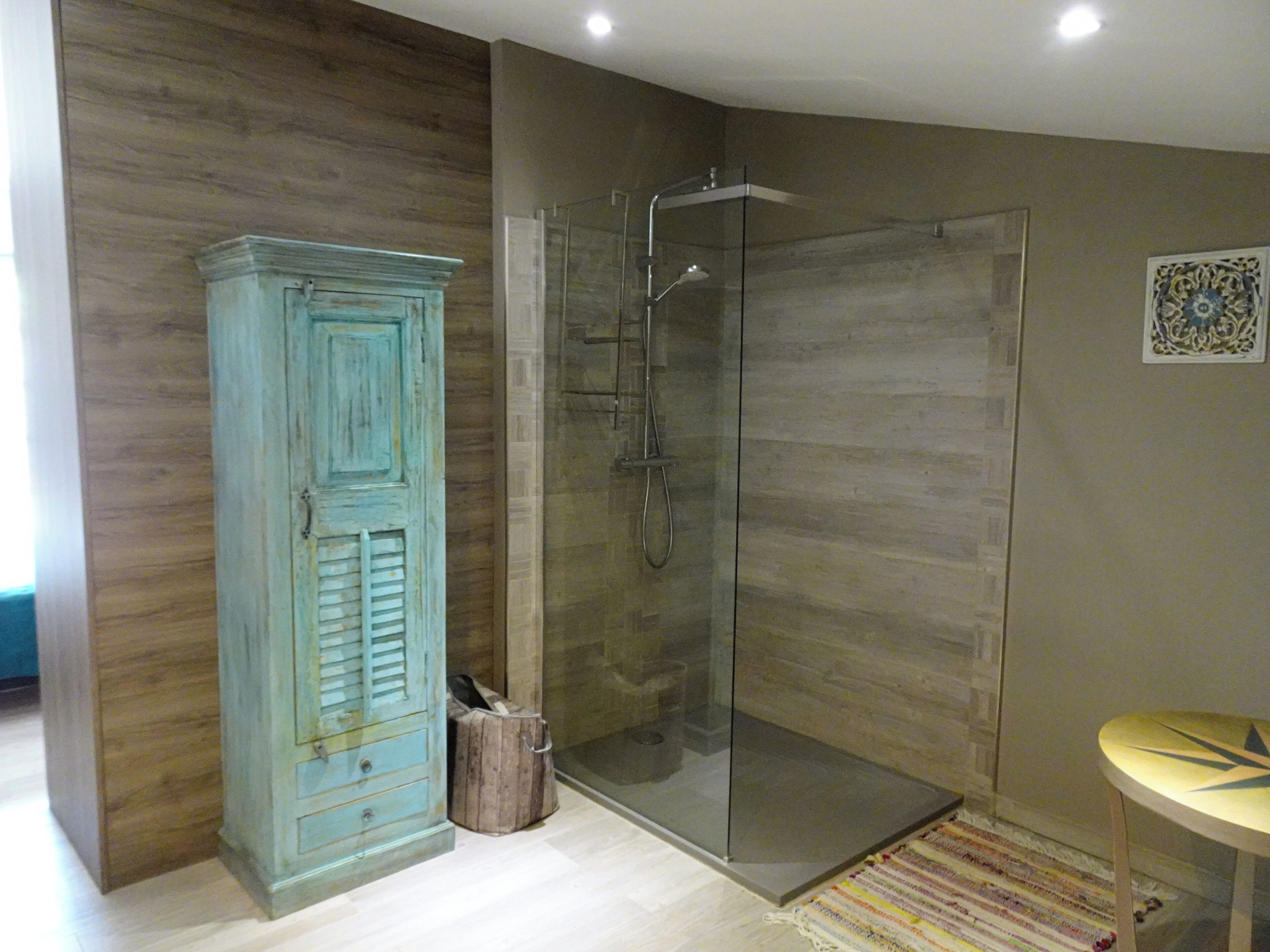 A bathroom with a glass shower enclosure, a wooden cabinet, and a small round table.