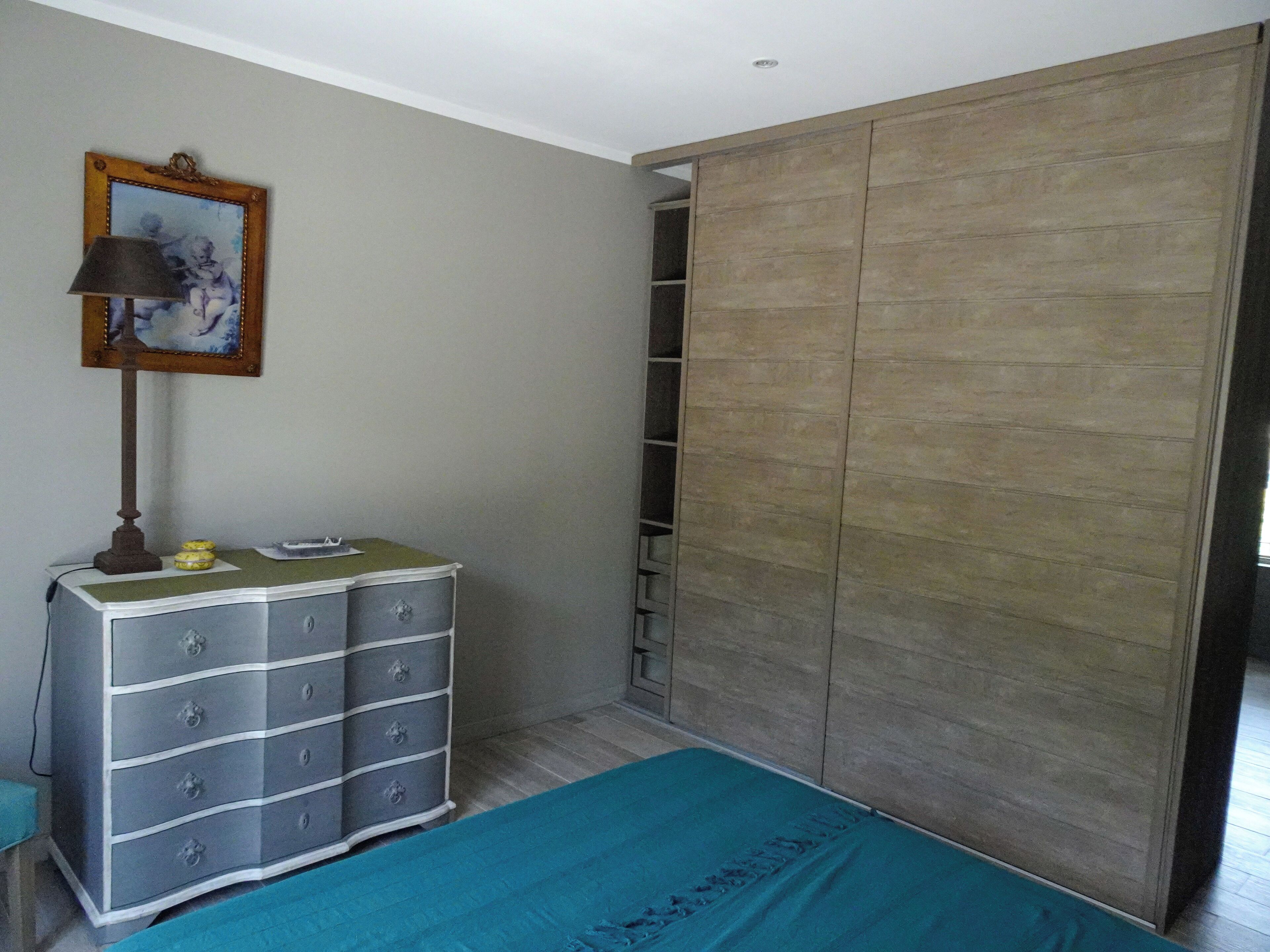 Une chambre à coucher avec un lit, une commode, une armoire et un tableau accroché au mur.