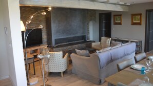A living room with a fireplace, a television, and a dining area with a table set for two. - Luxury Villa, Pool and Beautiful View (Saint-Raphaël)